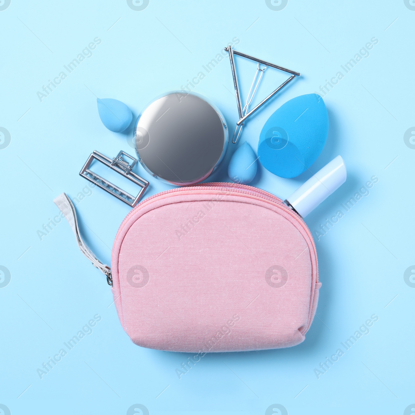 Photo of Cosmetic bag with makeup products and beauty accessories on light blue background, flat lay