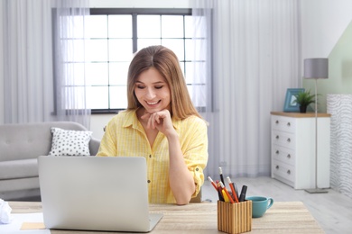 Photo of Young woman working with laptop at desk in home office