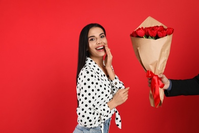 Photo of Happy woman receiving tulip bouquet from man on red background. 8th of March celebration