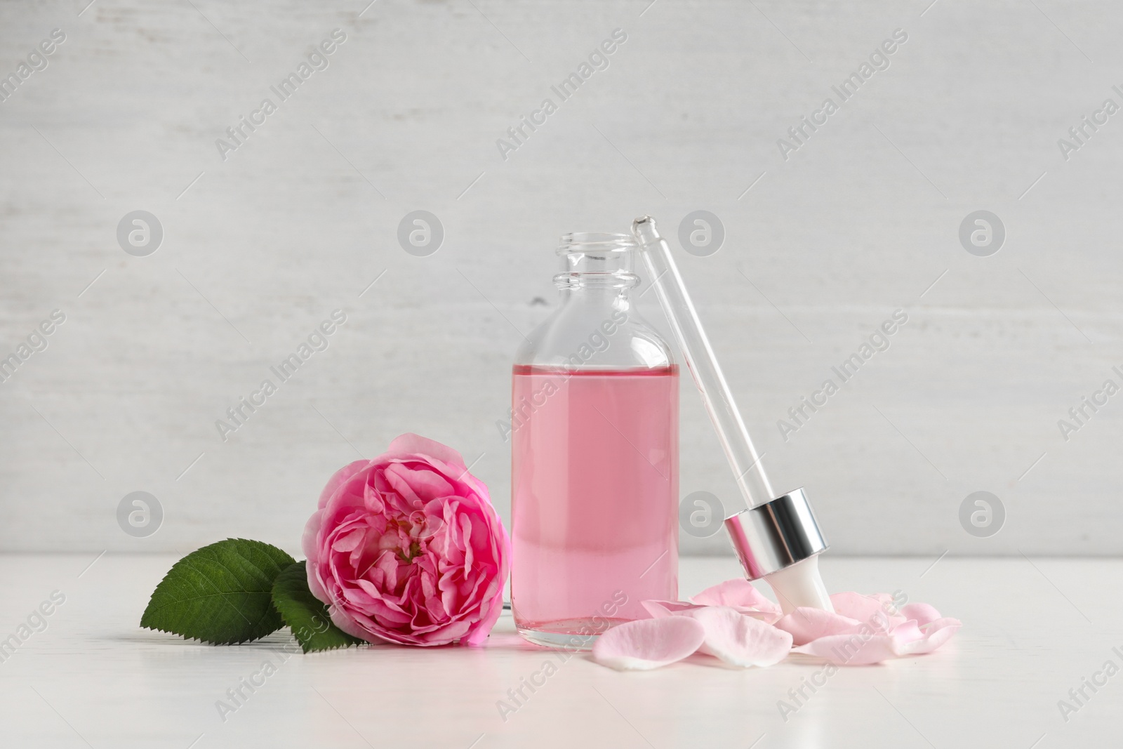 Photo of Fresh flower, bottle of rose essential oil and pipette on white table