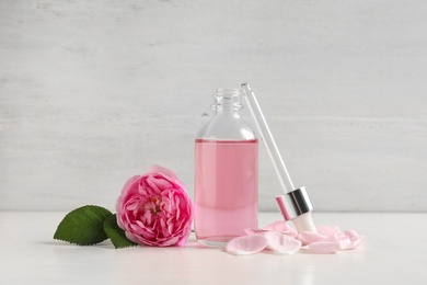 Photo of Fresh flower, bottle of rose essential oil and pipette on white table