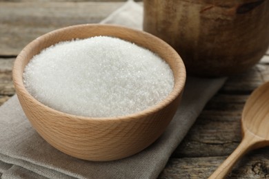 Photo of Granulated sugar in bowl on wooden table, closeup