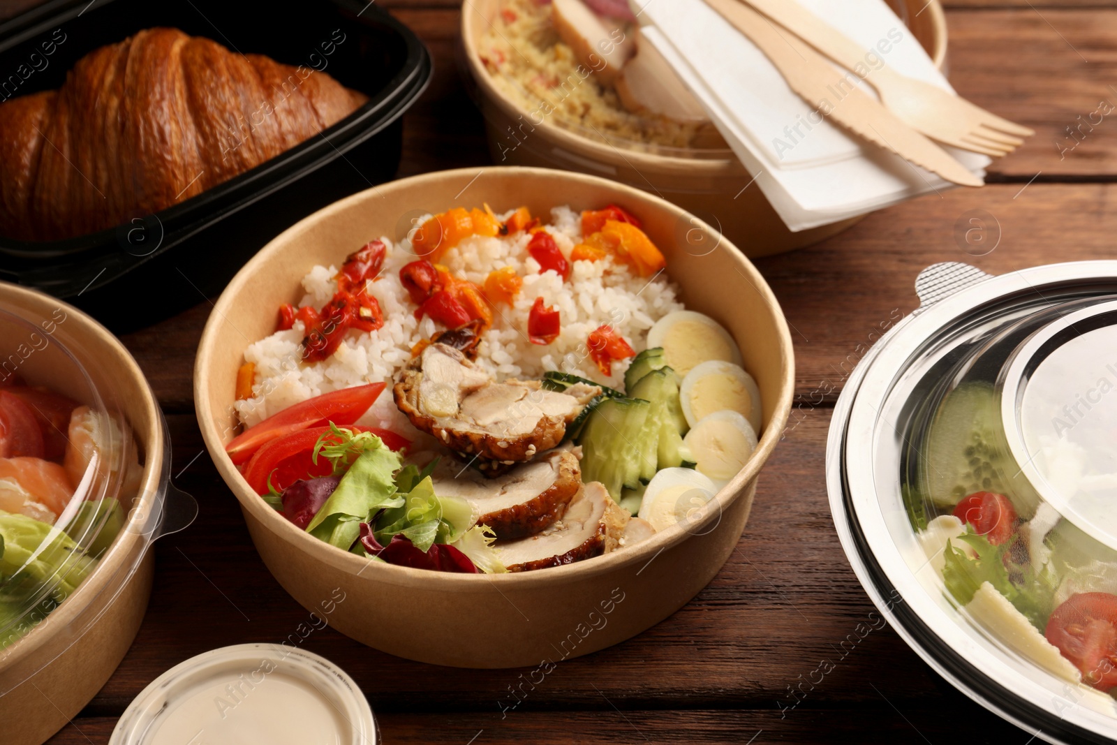 Photo of Tasty food in containers with knife and fork on wooden table