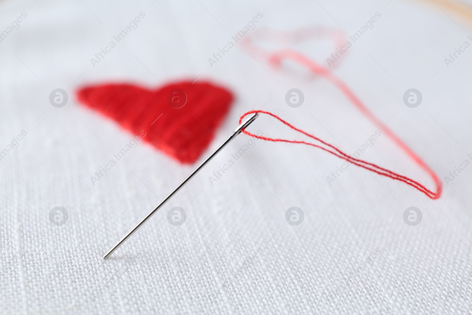Photo of Embroidered red hearts and needle on white cloth, closeup