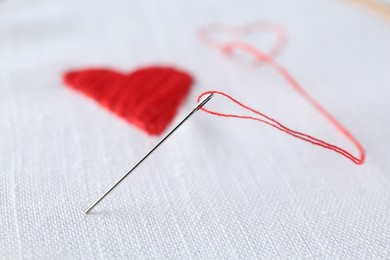 Embroidered red hearts and needle on white cloth, closeup