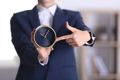 Businesswoman holding alarm clock on blurred background. Time concept