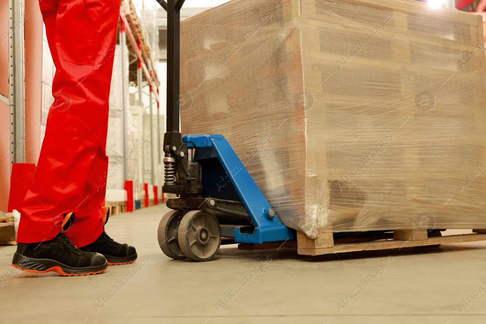 Image of Worker moving wrapped wooden pallets with manual forklift in warehouse, closeup