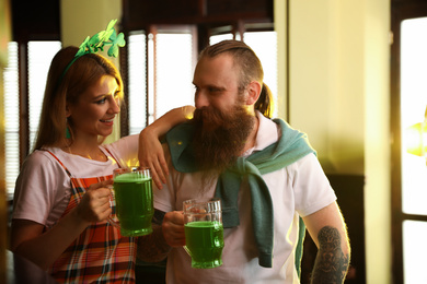 Photo of Young woman and man with glasses of green beer in pub. St. Patrick's Day celebration