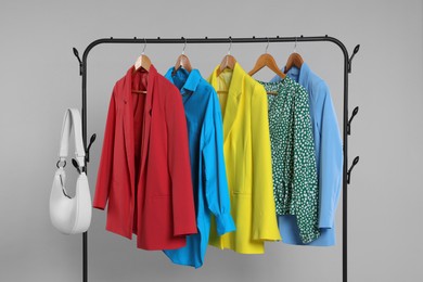Photo of Rack with bag and stylish women`s clothes on wooden hangers against light grey background