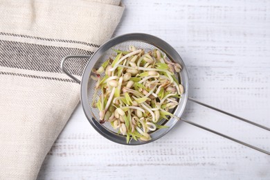 Photo of Mung bean sprouts in strainer and kitchen towel on white wooden table, top view