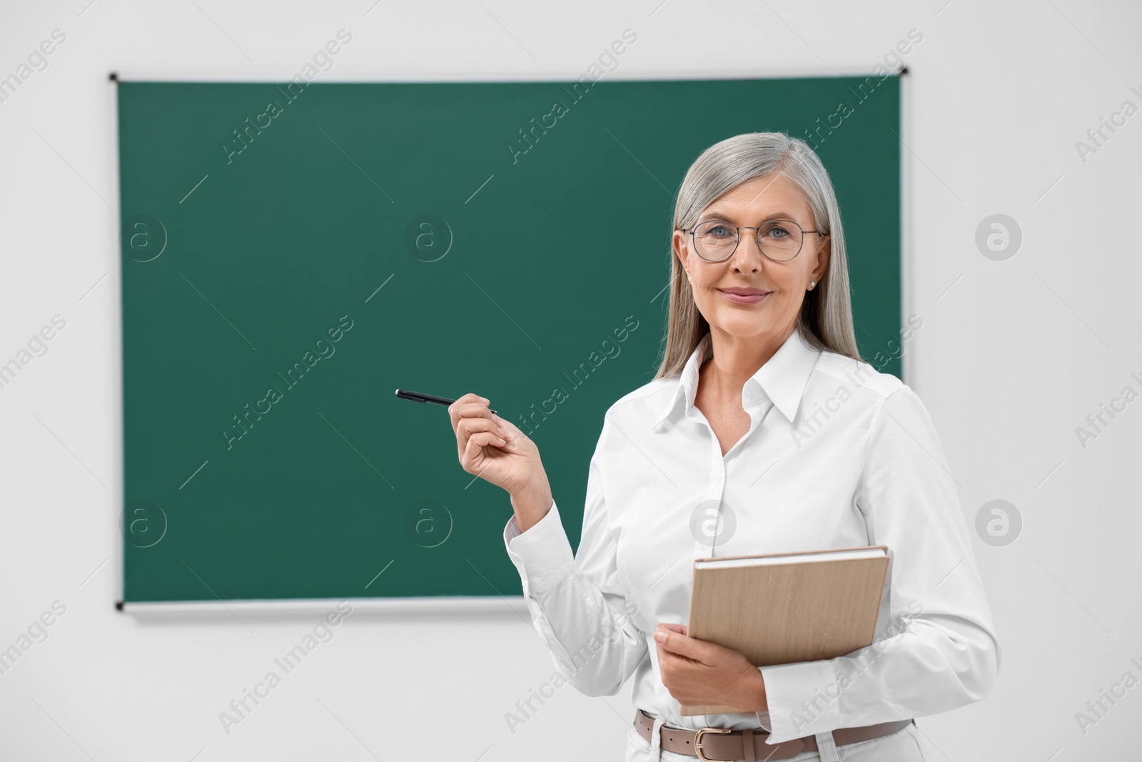 Photo of Portrait of professor with pen and notebook near blackboard in classroom, space for text