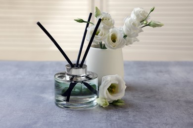 Reed diffuser and vase with eustoma flowers on gray marble table