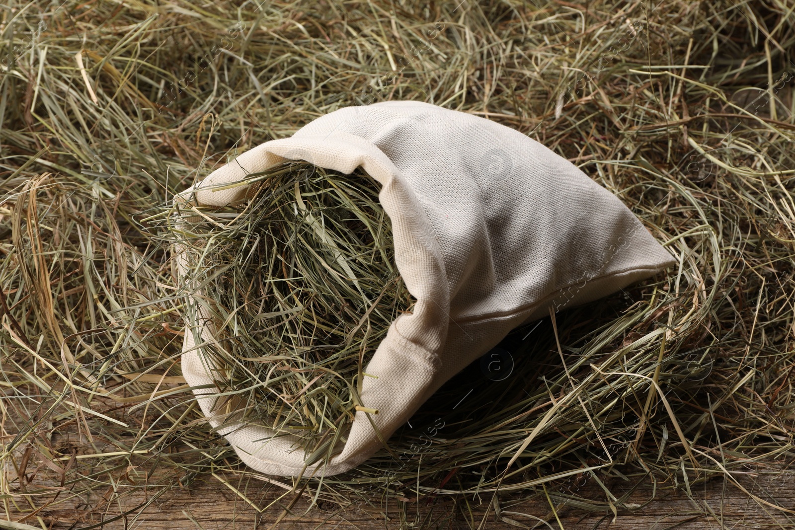 Photo of Dried hay in burlap sack on wooden table, closeup