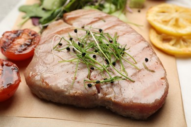 Photo of Delicious tuna steak with microgreens on parchment paper, closeup