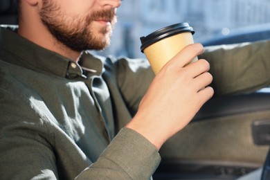 Coffee to go. Man with paper cup of drink in car, closeup