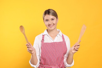 Photo of Beautiful young woman in clean striped apron with kitchen tools on orange background