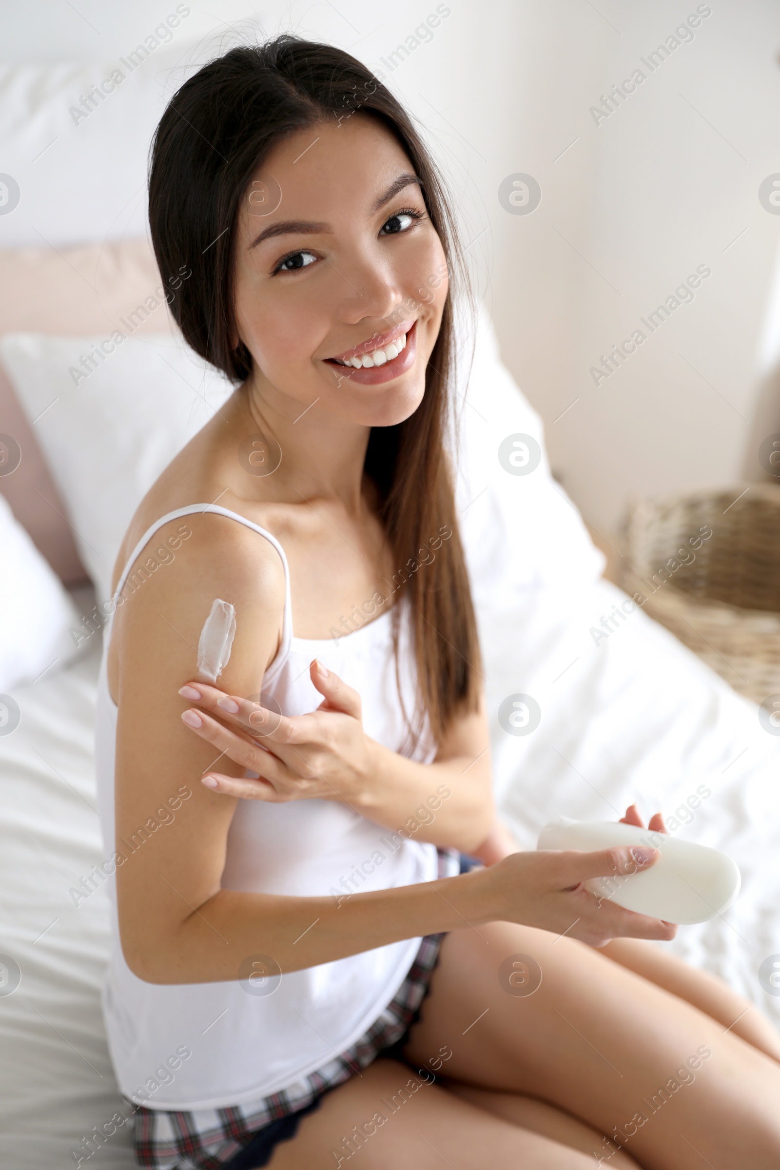 Photo of Beautiful young woman applying body cream in bedroom