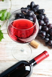 Photo of Glass and bottle of red wine with fresh ripe juicy grapes on table