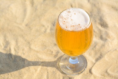 Photo of Glass of cold beer on sandy beach, closeup. Space for text