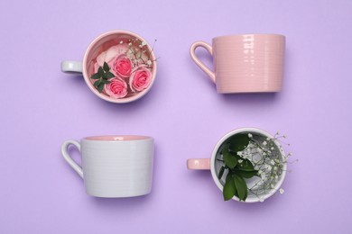 Photo of Cups with flowers on violet background, flat lay