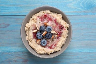 Photo of Tasty oatmeal porridge with toppings on light blue wooden table, top view