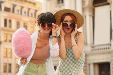 Photo of Happy friends with pink cotton candy outdoors on sunny day