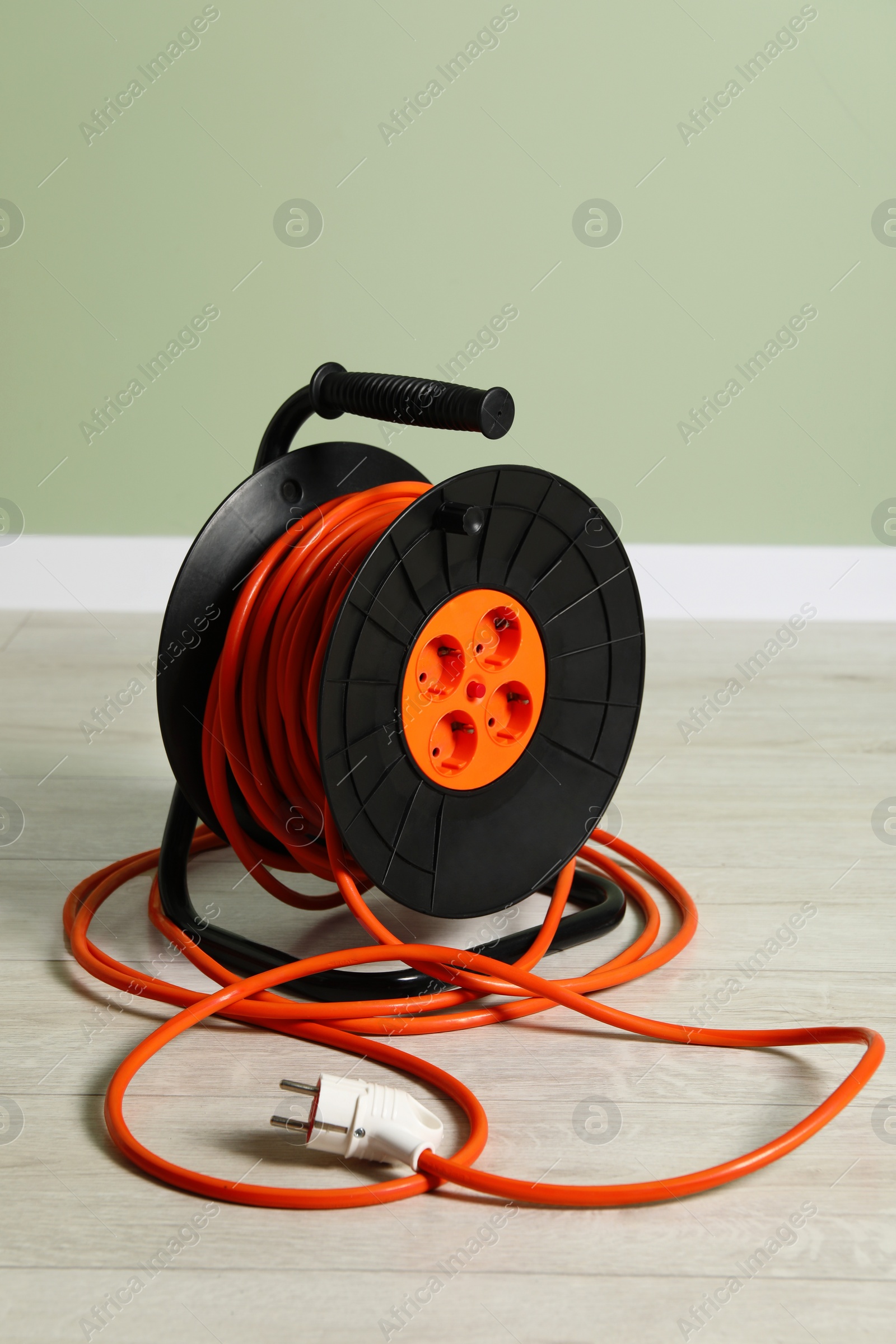 Photo of Extension cord reel on floor near light green wall. Electrician's equipment