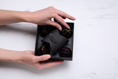 Photo of Woman holding box of delicious chocolate candies on white marble table, top view