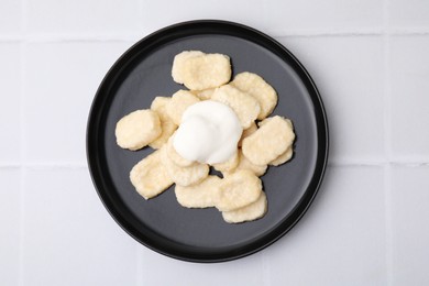 Photo of Plate of tasty lazy dumplings with sour cream on white tiled table, top view