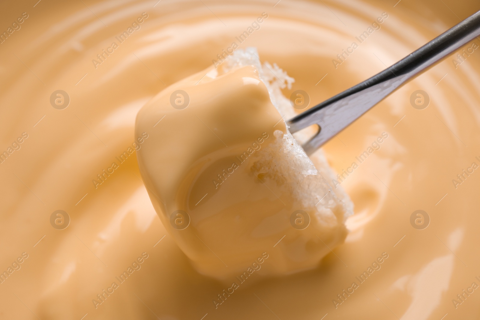 Photo of Dipping bread into tasty cheese fondue, closeup