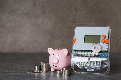 Photo of Electricity meter, piggy bank and coins on grey table. Space for text