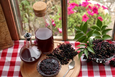 Elderberry drink and jam with Sambucus berries on table near window