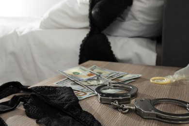Photo of Prostitution concept. Handcuffs, black panties, dollar banknotes and condom on wooden table indoors, closeup with space for text