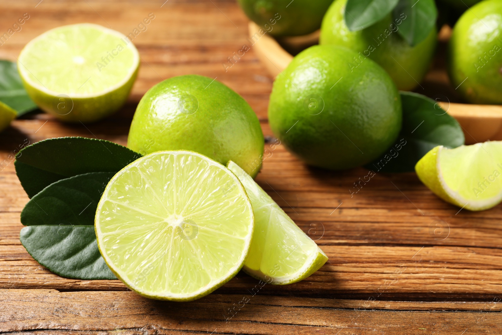 Photo of Fresh ripe limes and green leaves on wooden table, closeup