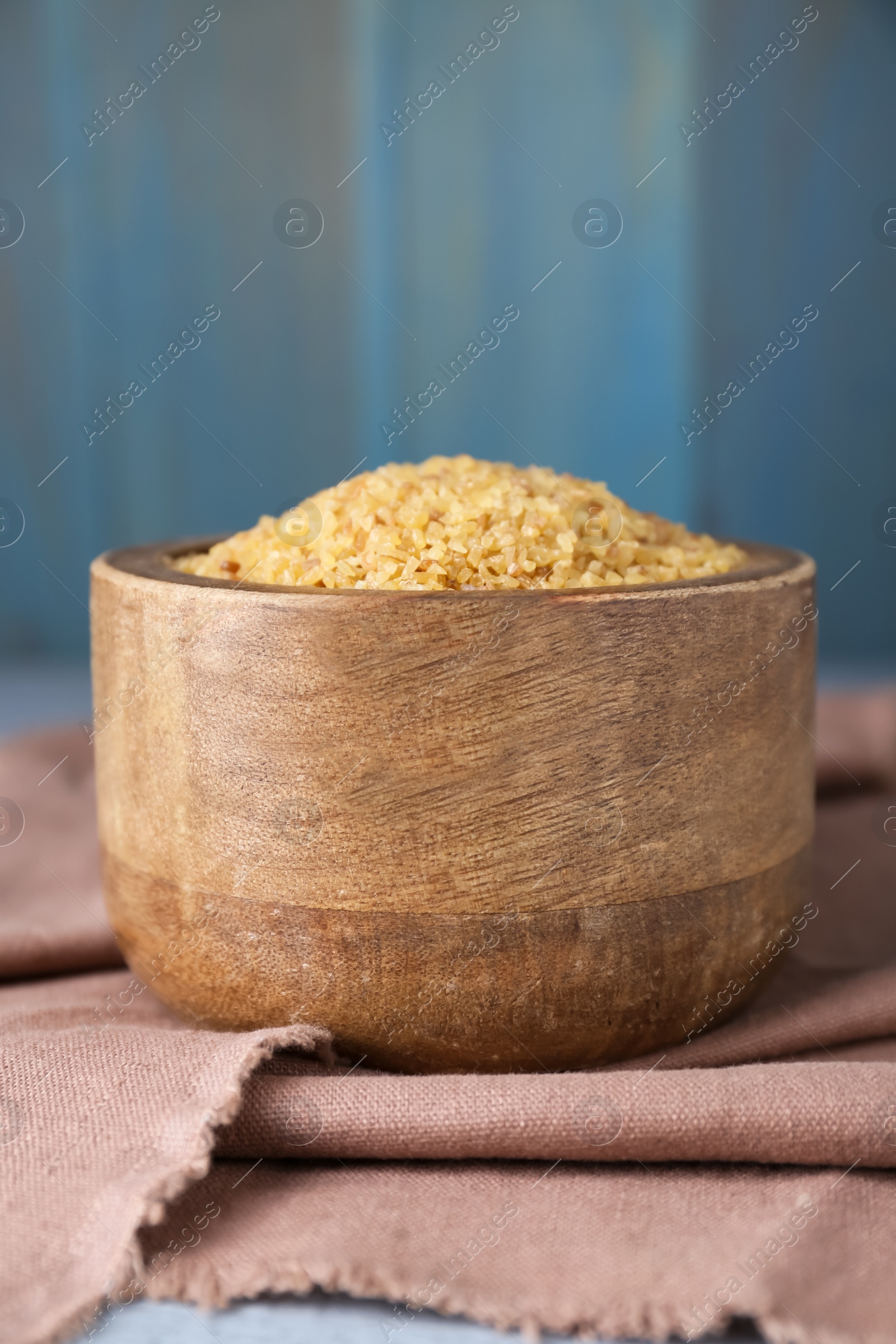 Photo of Bowl with uncooked bulgur and napkin on table, closeup