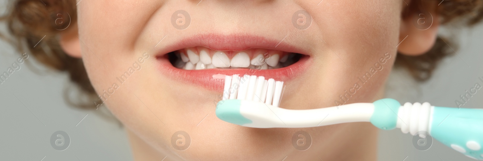 Image of Little boy brushing his teeth with plastic toothbrush on light grey background, closeup. Banner design
