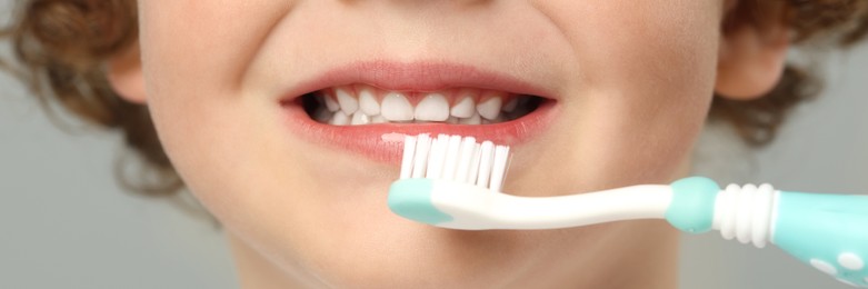 Little boy brushing his teeth with plastic toothbrush on light grey background, closeup. Banner design