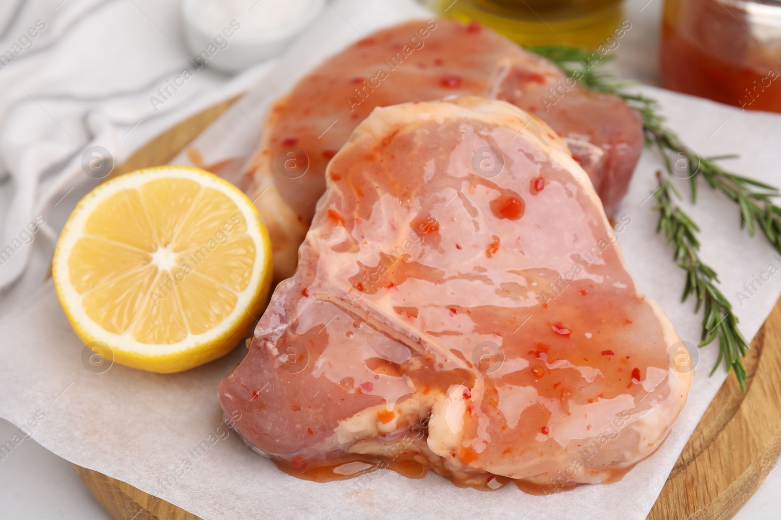 Photo of Board with raw marinated meat, lemon and rosemary on white table, closeup