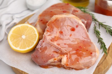 Photo of Board with raw marinated meat, lemon and rosemary on white table, closeup