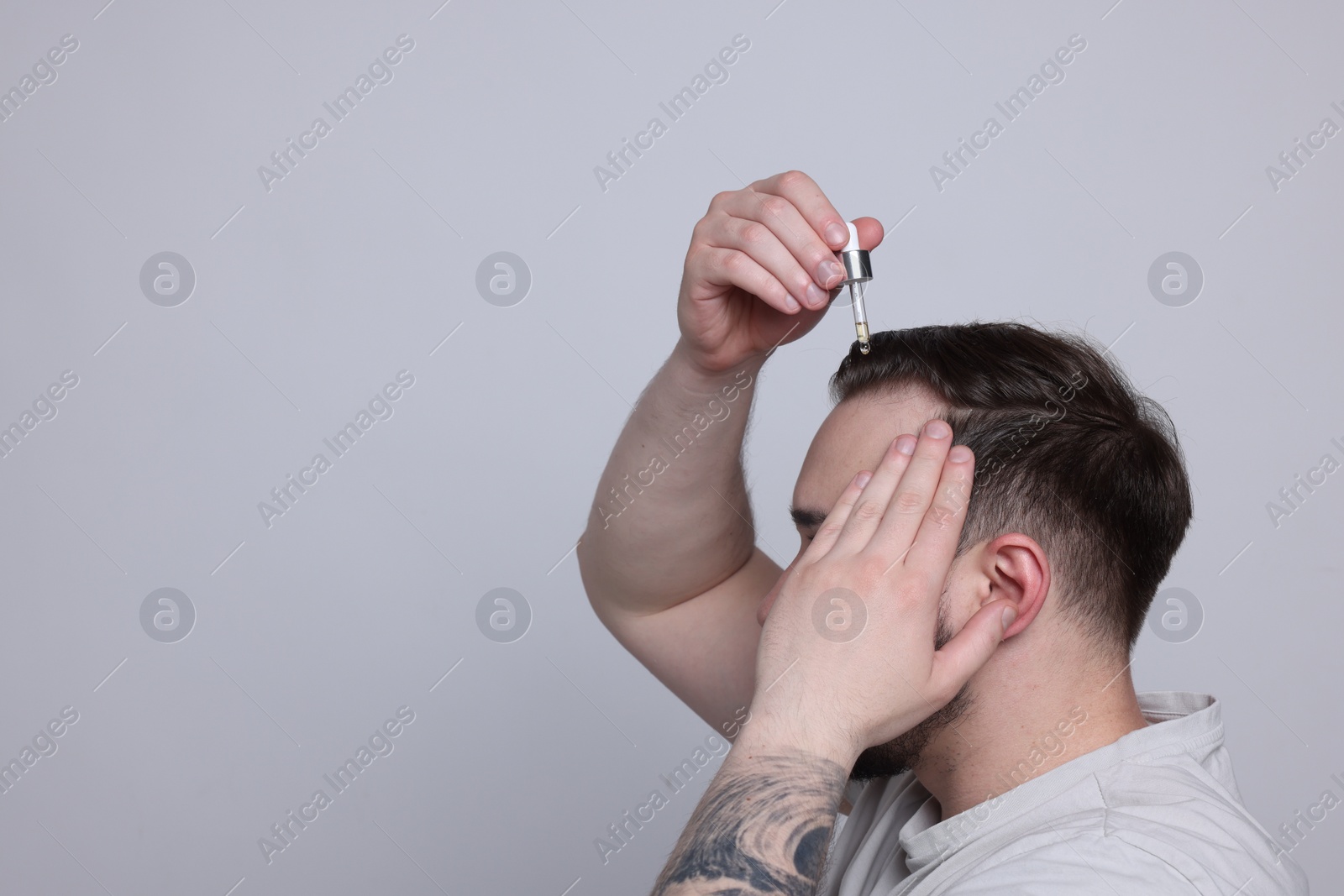 Photo of Baldness concept. Man dripping serum onto his hair on light grey background, space for text