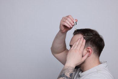 Photo of Baldness concept. Man dripping serum onto his hair on light grey background, space for text