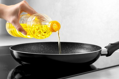 Photo of Woman pouring cooking oil from bottle into frying pan on stove, closeup