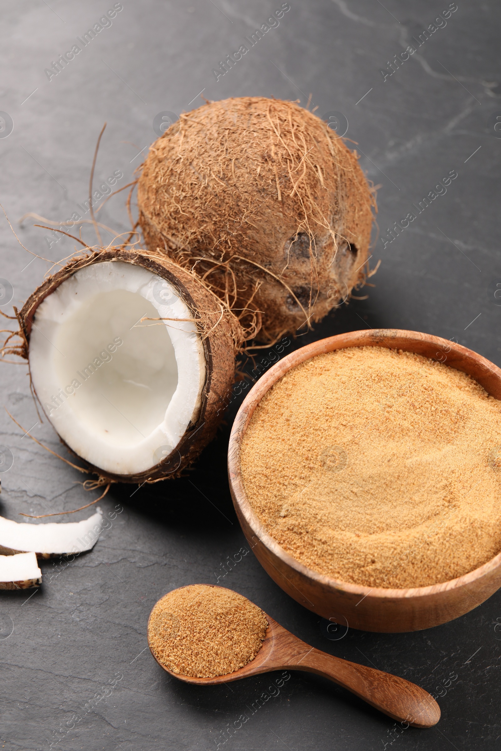 Photo of Spoon with coconut sugar, bowl and fruits on dark textured table, closeup