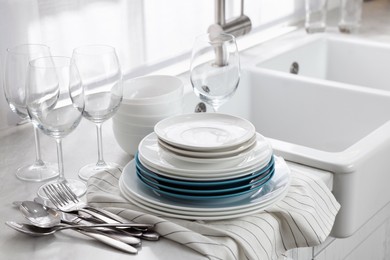 Photo of Different clean dishware, cutlery and glasses on countertop near sink in kitchen