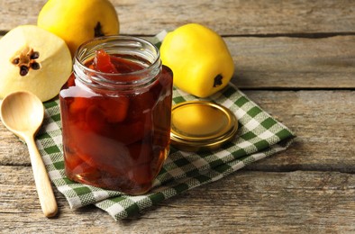 Tasty homemade quince jam in jar, spoon and fruits on wooden table, closeup. Space for text