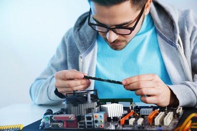 Photo of Male technician repairing motherboard at table against light background