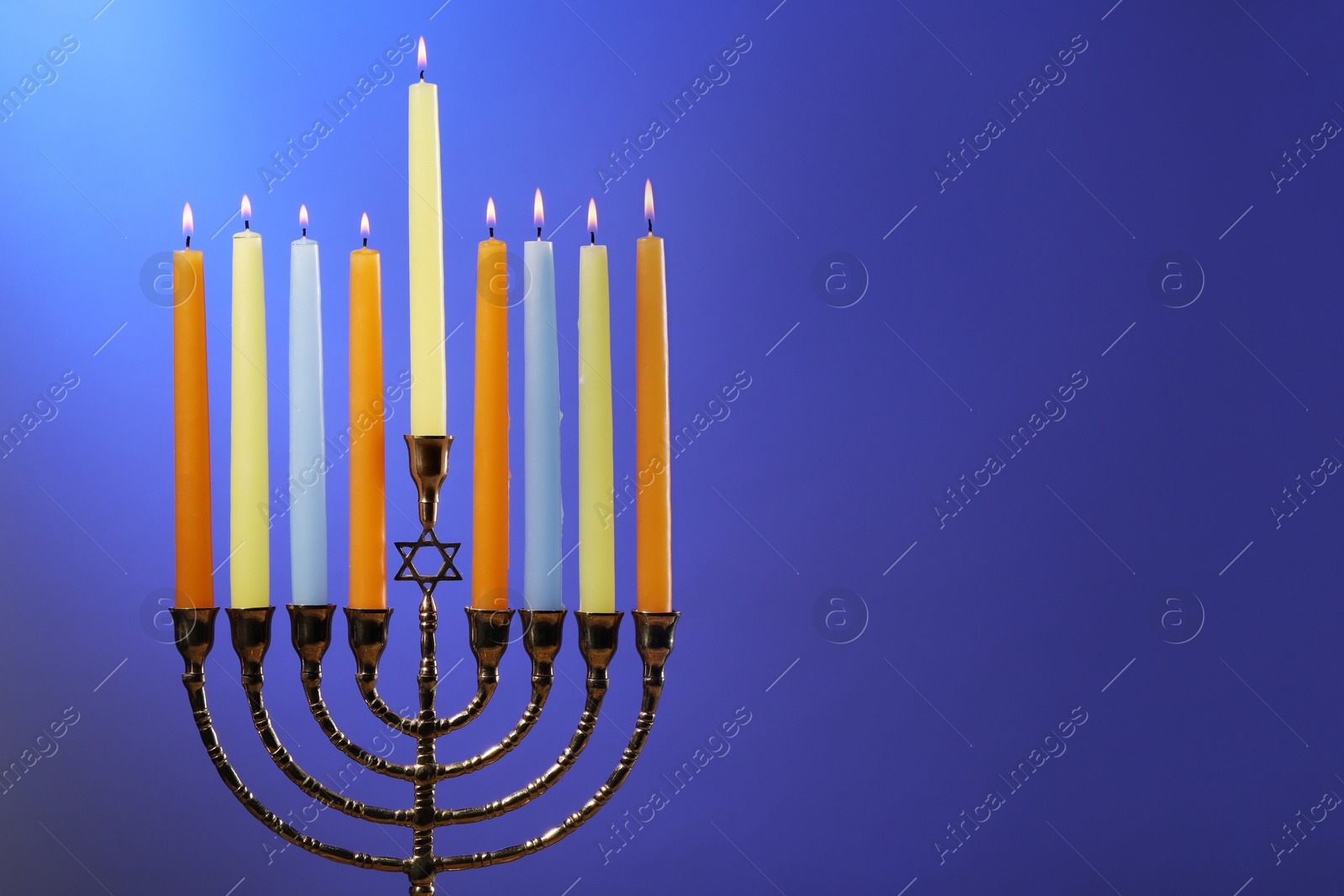 Photo of Hanukkah celebration. Menorah with burning candles on blue background, space for text