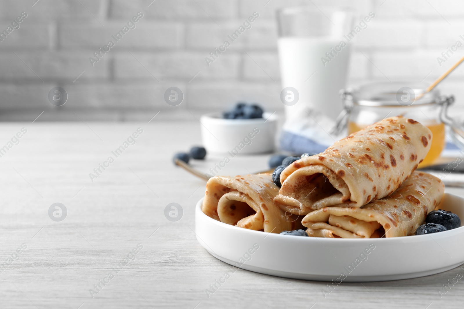 Photo of Delicious crepes with blueberries on white wooden table. Space for text