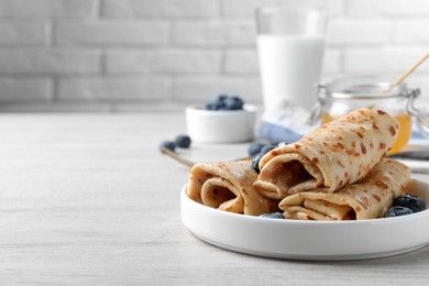 Photo of Delicious crepes with blueberries on white wooden table. Space for text