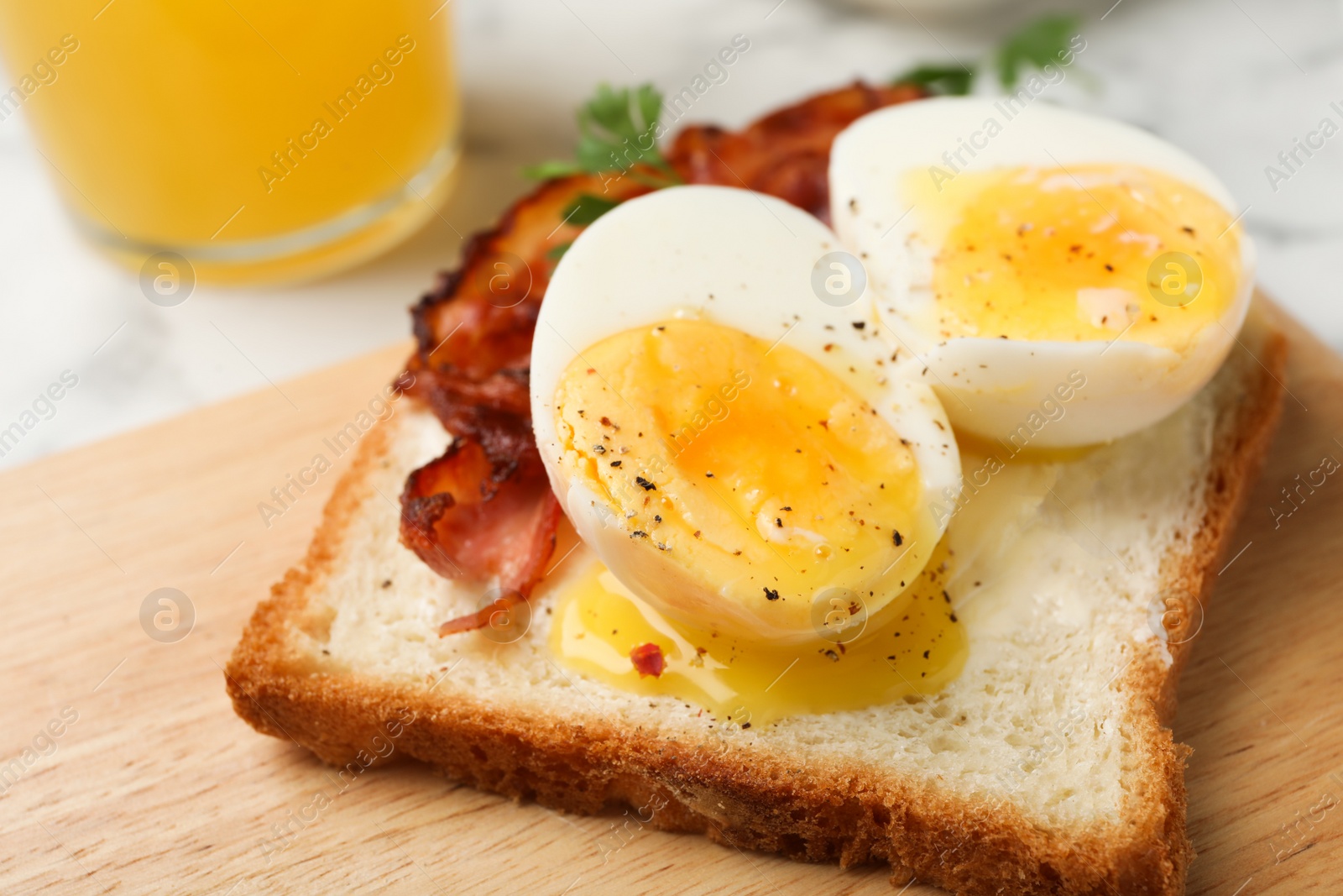 Photo of Toast with soft boiled egg and bacon on wooden board, closeup